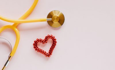 From above of yellow stethoscope near small red bead heart made for San Valentines Day on pale pink surface — CompareMedicare