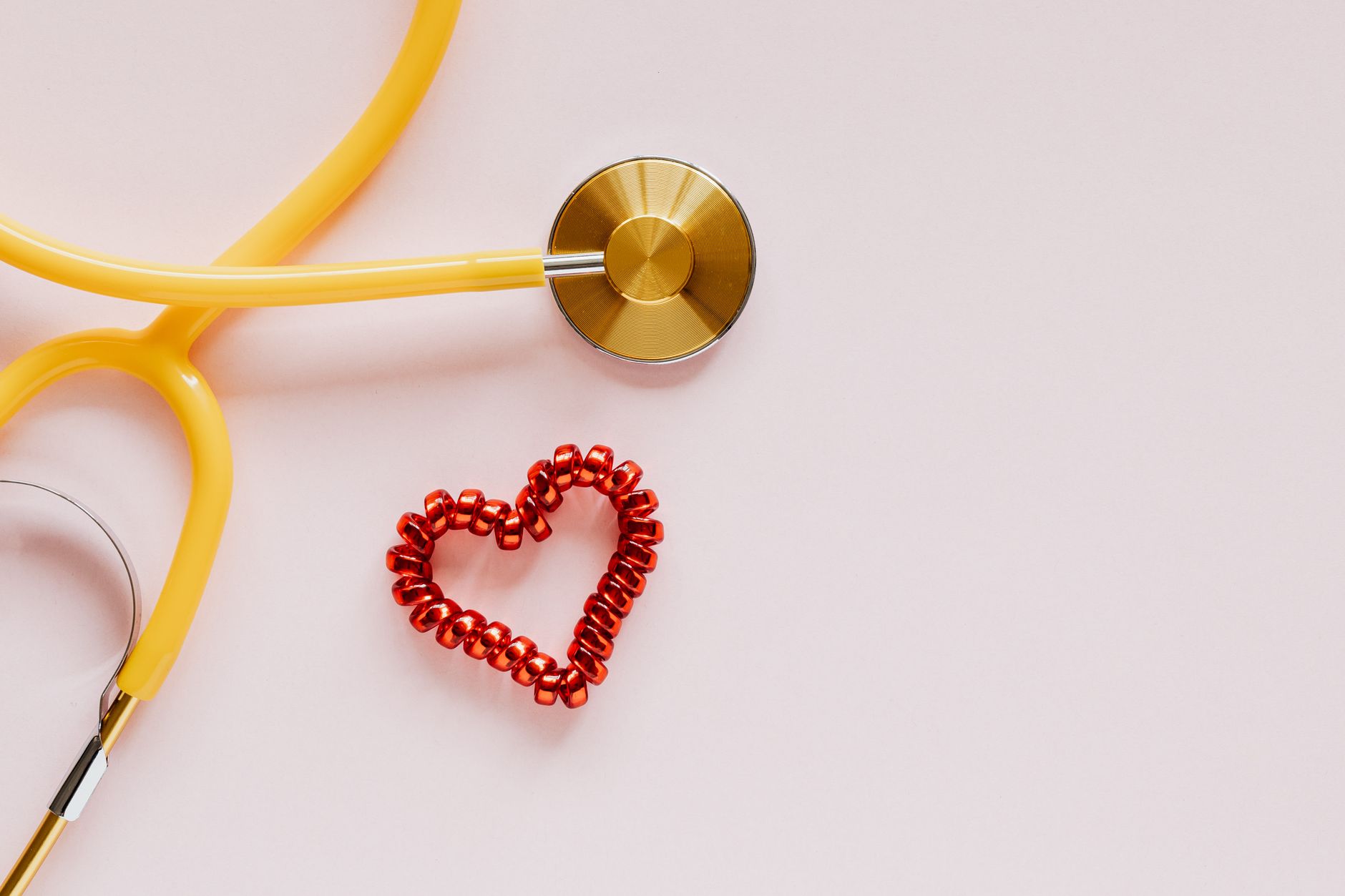 From above of yellow stethoscope near small red bead heart made for San Valentines Day on pale pink surface — CompareMedicare